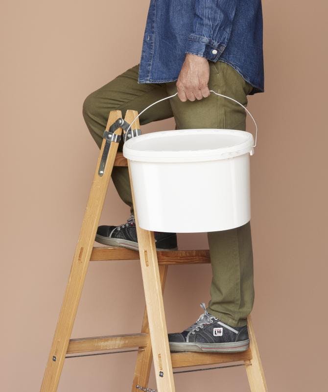 Man on a ladder holding a white ALPLAindustrial bucket